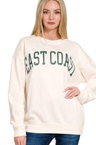 Woman wearing a cream sweatshirt with 'East Coast' text on a white background