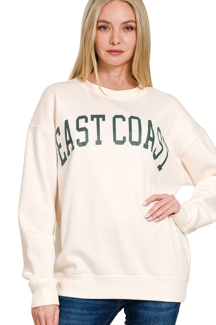 Woman wearing a cream sweatshirt with 'East Coast' text on a white background